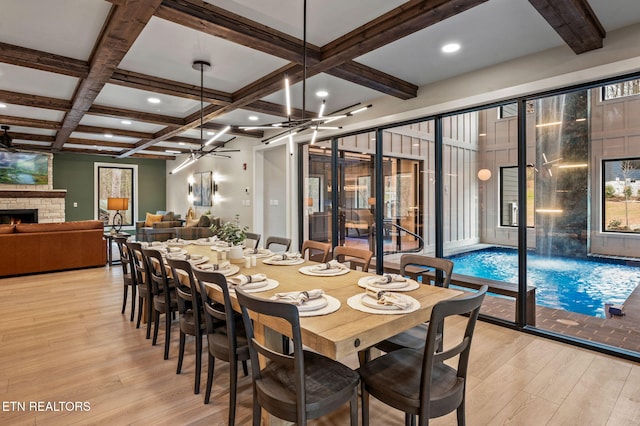 dining space featuring light wood finished floors, beam ceiling, coffered ceiling, and a stone fireplace