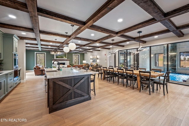 dining space featuring beam ceiling, light wood-style floors, a warm lit fireplace, and coffered ceiling