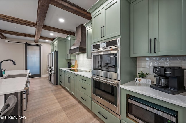 kitchen featuring a sink, a barn door, stainless steel appliances, green cabinetry, and custom exhaust hood