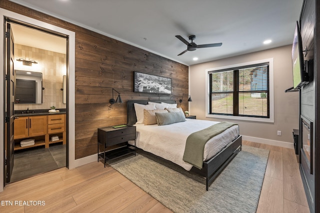 bedroom featuring baseboards, wood walls, light wood-type flooring, recessed lighting, and a sink