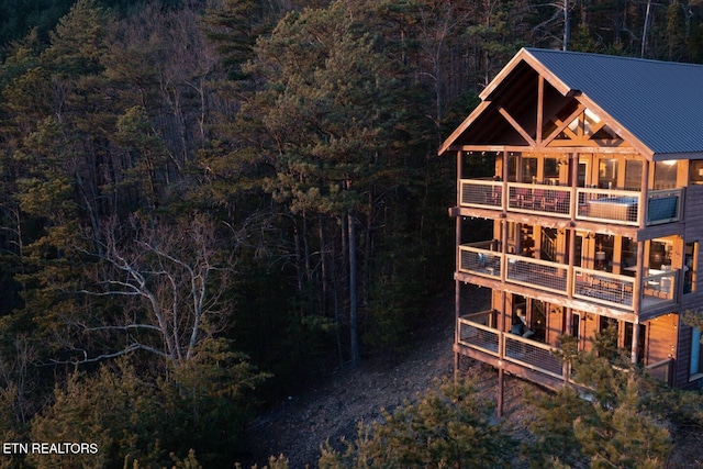 exterior space featuring a balcony, metal roof, and a view of trees