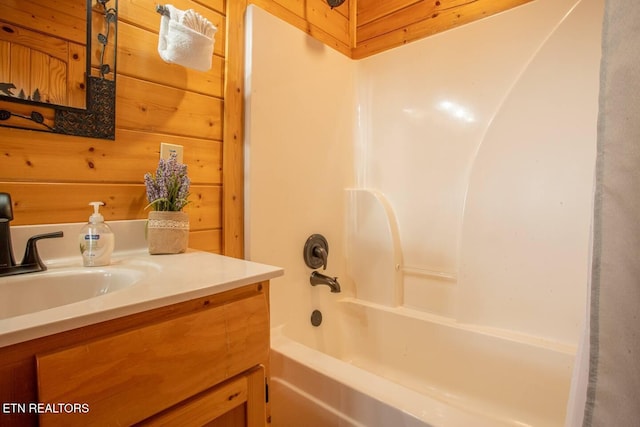 bathroom with tub / shower combination, wood walls, and vanity