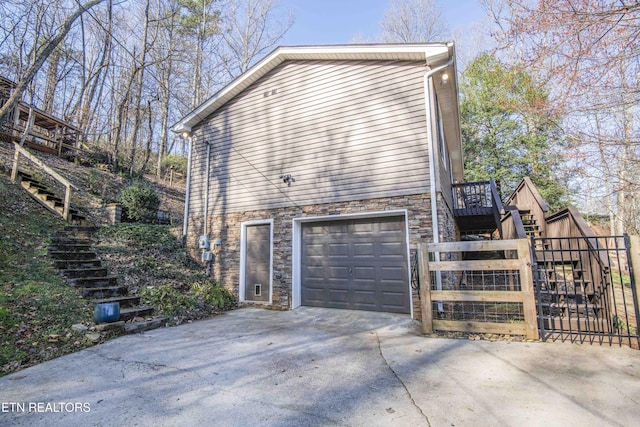 view of property exterior with fence, stairway, concrete driveway, a garage, and stone siding