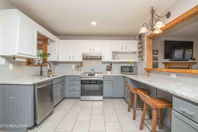 kitchen with open shelves, a sink, gray cabinetry, under cabinet range hood, and appliances with stainless steel finishes