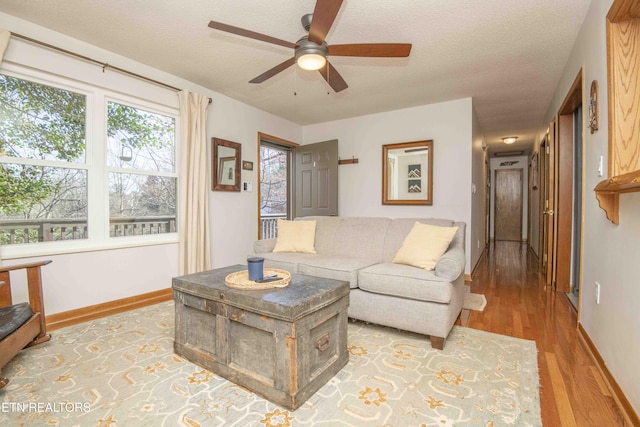 living area featuring a textured ceiling, a ceiling fan, baseboards, and wood finished floors