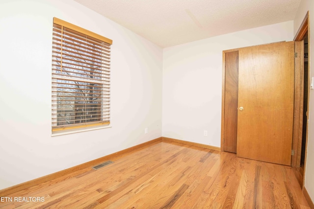 unfurnished bedroom with light wood-type flooring, visible vents, baseboards, and a textured ceiling