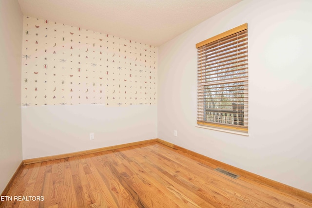 spare room featuring wood finished floors, visible vents, and baseboards