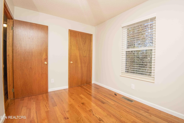 unfurnished bedroom with visible vents, baseboards, wood finished floors, a closet, and a textured ceiling