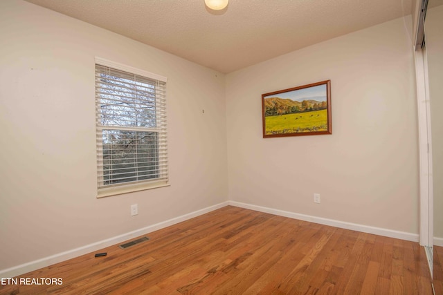 unfurnished room featuring visible vents, baseboards, a textured ceiling, and wood finished floors