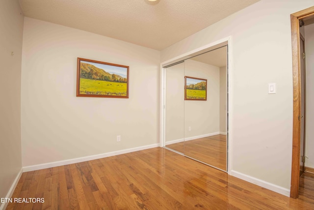 unfurnished bedroom with a closet, baseboards, a textured ceiling, and wood finished floors