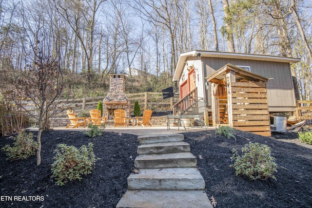 exterior space featuring a patio, fence, an outdoor structure, and an outdoor stone fireplace