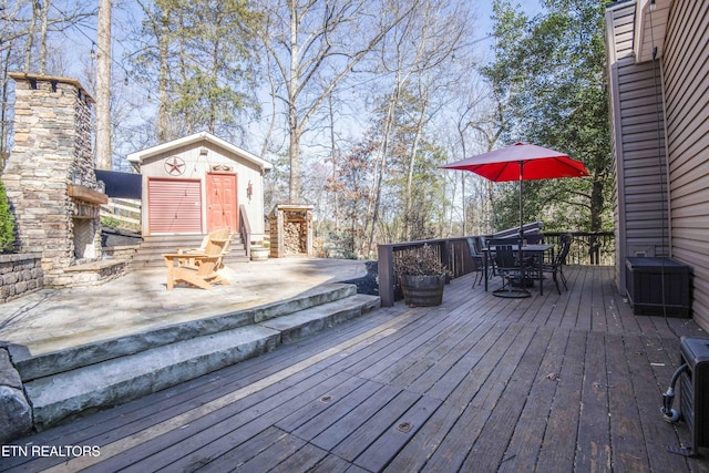 deck featuring an outbuilding, an outdoor stone fireplace, and outdoor dining space