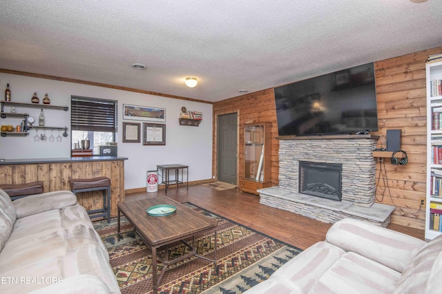 living area with a stone fireplace, crown molding, wood finished floors, and a textured ceiling