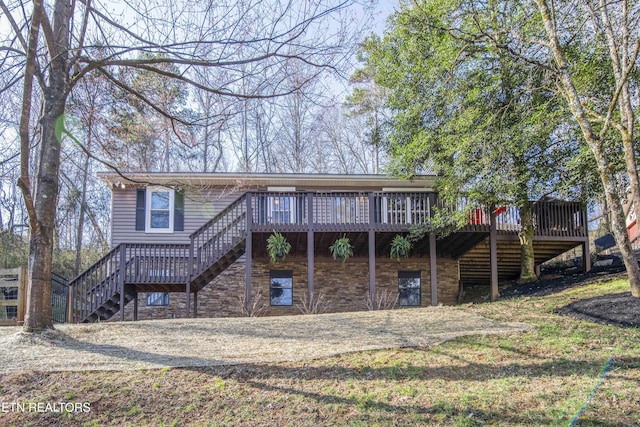 back of property featuring stairs, a deck, stone siding, and driveway