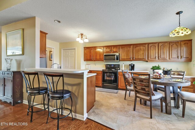 kitchen featuring stainless steel microwave, a breakfast bar, brown cabinets, a peninsula, and black electric range oven