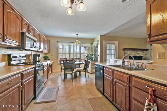 kitchen with black appliances, a sink, decorative light fixtures, a fireplace, and light countertops