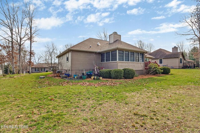 rear view of property featuring a chimney, roof with shingles, a yard, and a sunroom