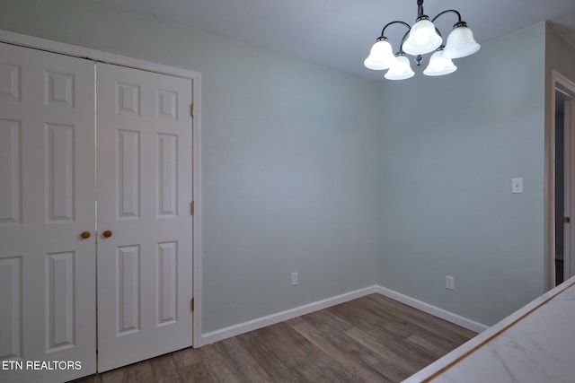 empty room featuring baseboards, wood finished floors, and a notable chandelier