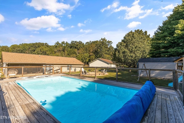 view of swimming pool featuring fence, a shed, a wooden deck, a yard, and an outdoor structure