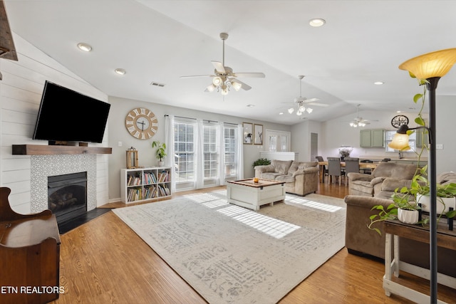 living area featuring light wood-type flooring, visible vents, recessed lighting, lofted ceiling, and a tile fireplace