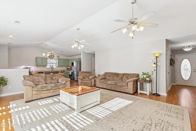 living room featuring visible vents, baseboards, lofted ceiling, light wood-style flooring, and a ceiling fan