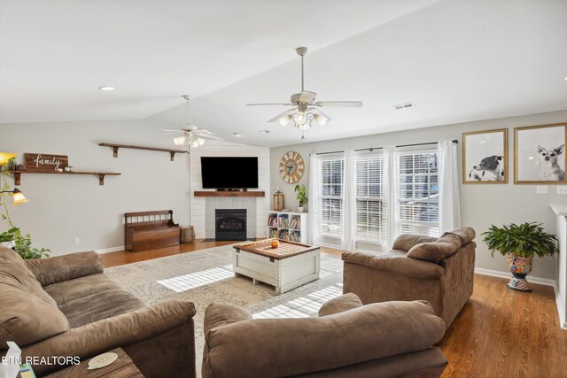 living room featuring vaulted ceiling, wood finished floors, baseboards, and a large fireplace