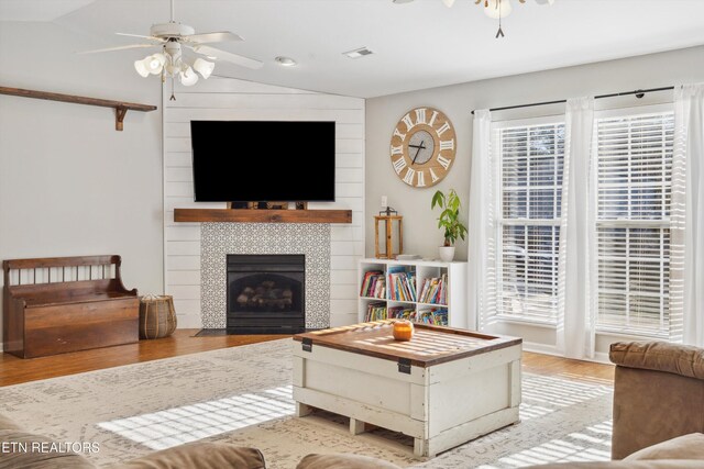 living room featuring visible vents, a tiled fireplace, wood finished floors, lofted ceiling, and ceiling fan