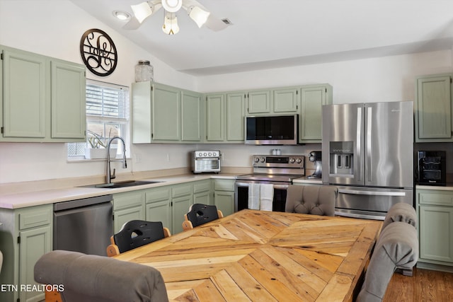 kitchen featuring green cabinetry, stainless steel appliances, light countertops, and a sink