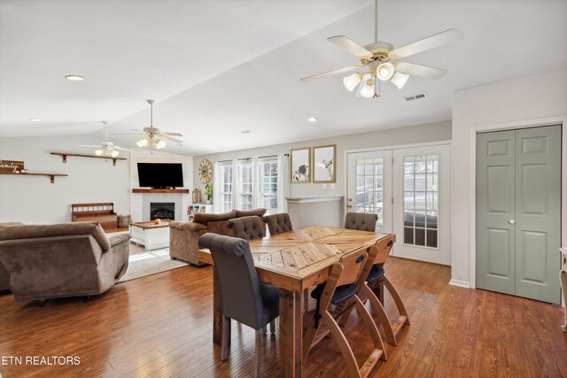 dining room with wood finished floors, visible vents, a ceiling fan, a fireplace, and vaulted ceiling