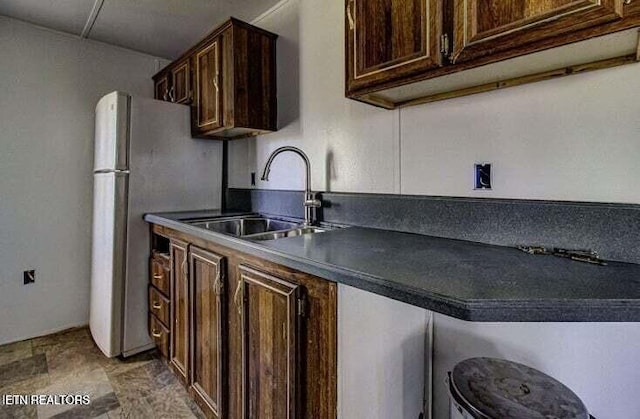 kitchen featuring freestanding refrigerator, dark countertops, a sink, and dark brown cabinetry