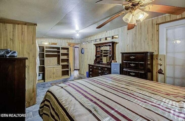 bedroom with wood walls, ceiling fan, and stone finish floor