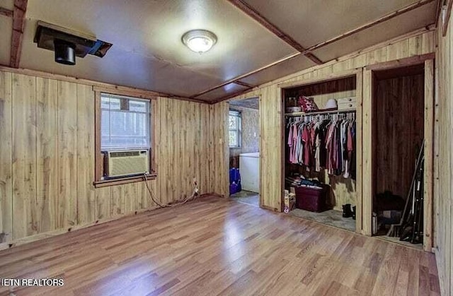 unfurnished bedroom with a closet, wood walls, cooling unit, and wood finished floors