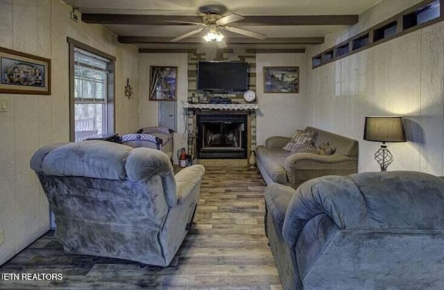 living room with a large fireplace, a ceiling fan, beamed ceiling, and wood finished floors