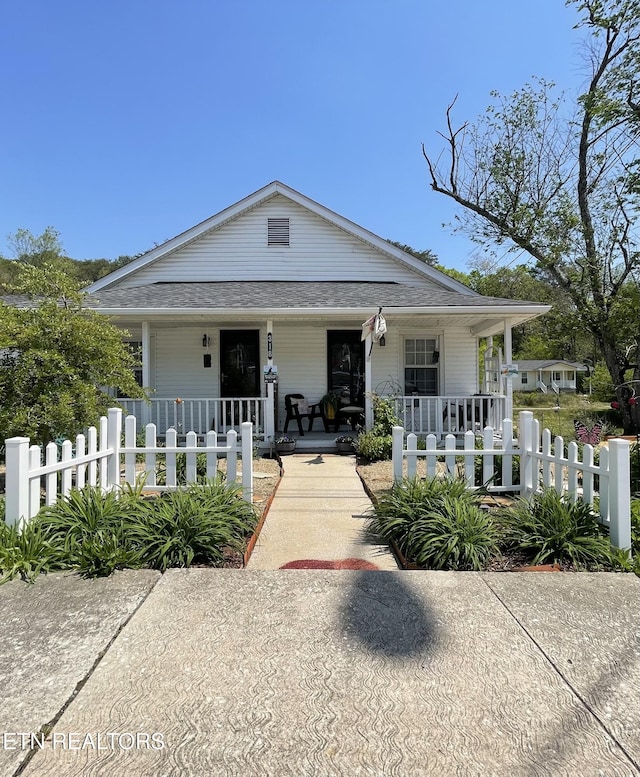 bungalow-style home with a porch, a fenced front yard, and roof with shingles