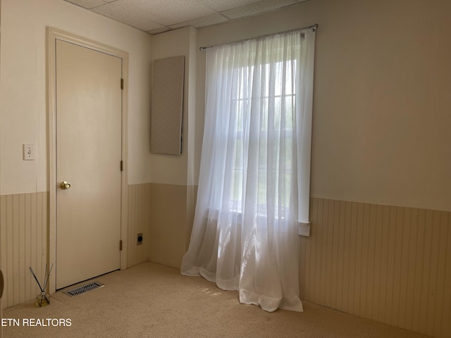 carpeted spare room featuring visible vents, wainscoting, and a drop ceiling