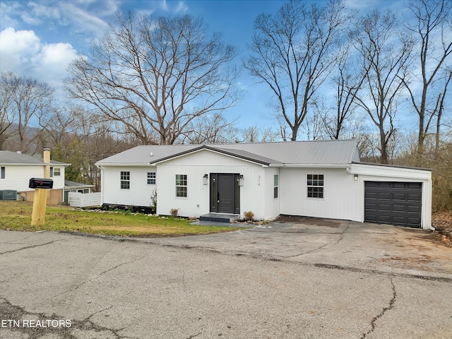 view of front of property with central air condition unit, a front yard, metal roof, a garage, and driveway