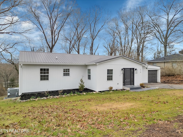 exterior space featuring a garage, metal roof, a lawn, and driveway