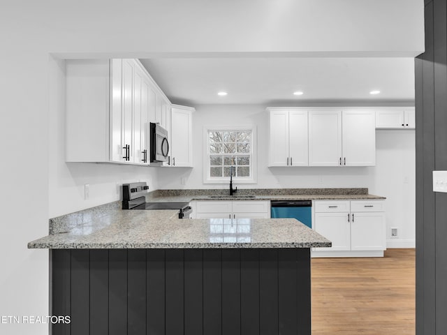 kitchen with a peninsula, a sink, light wood-style floors, white cabinets, and appliances with stainless steel finishes