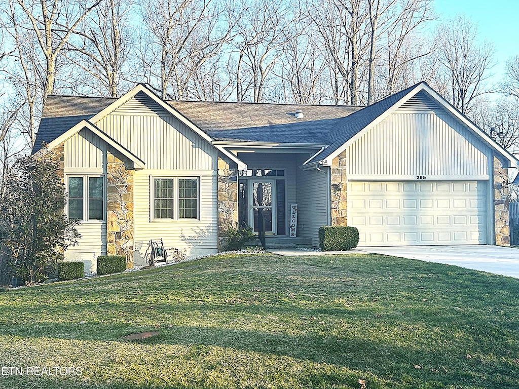 view of front of house with a front yard, an attached garage, concrete driveway, stone siding, and board and batten siding