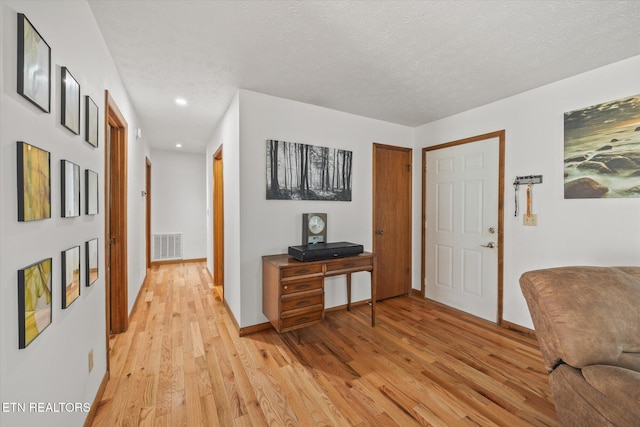 foyer entrance with a textured ceiling, baseboards, visible vents, and light wood-style floors