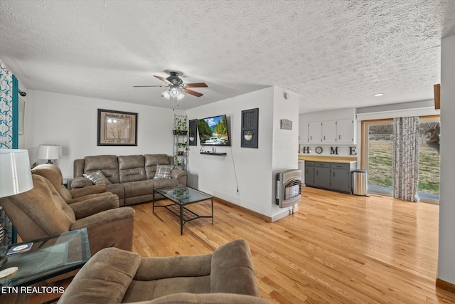 living room with a textured ceiling, light wood finished floors, a ceiling fan, and heating unit