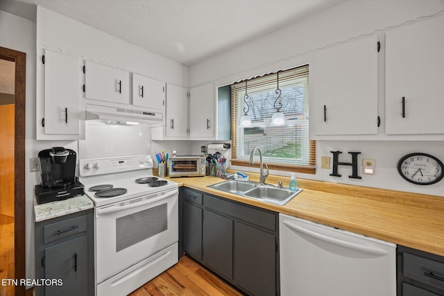 kitchen featuring white appliances, white cabinets, light countertops, under cabinet range hood, and a sink