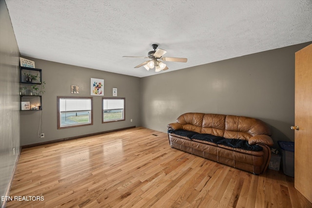 living room featuring a textured ceiling, ceiling fan, light wood-style flooring, and baseboards