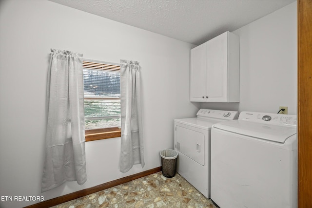 laundry area with a textured ceiling, washing machine and dryer, cabinet space, and baseboards