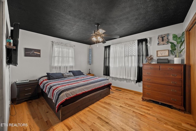 bedroom with light wood-style floors, a textured ceiling, baseboards, and a ceiling fan