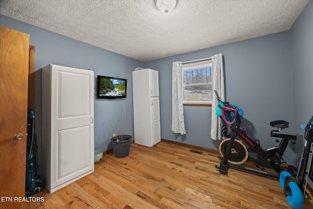 workout area featuring light wood-type flooring, visible vents, and a textured ceiling