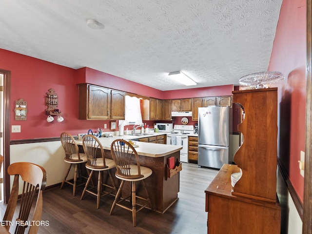 kitchen with a peninsula, white appliances, wood finished floors, and light countertops