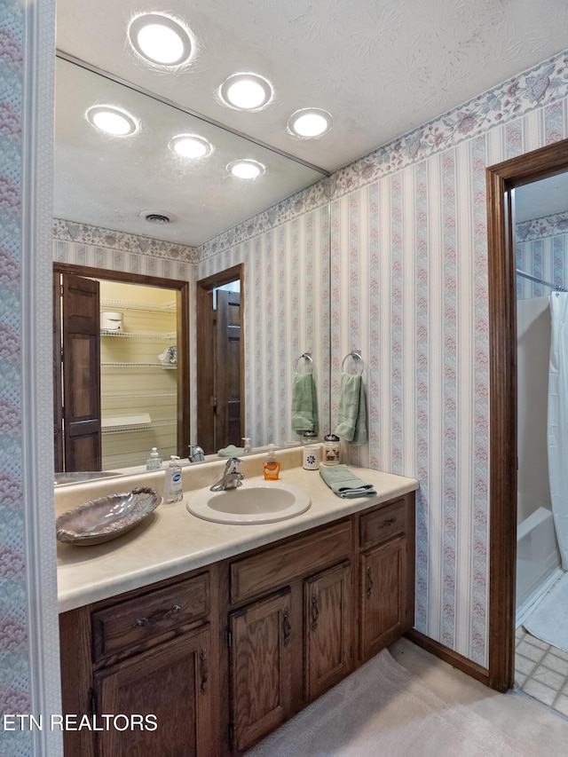 full bath featuring a textured ceiling, baseboards, vanity, and wallpapered walls