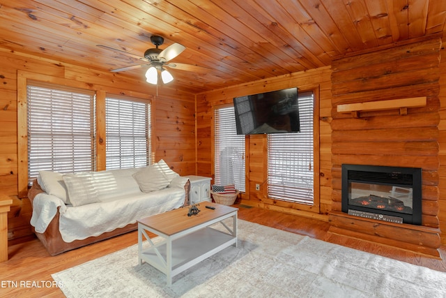 living area with a glass covered fireplace, wood ceiling, wooden walls, and wood finished floors