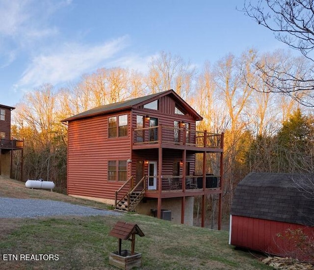 rear view of house featuring log veneer siding, an outbuilding, a shed, a wooden deck, and a yard